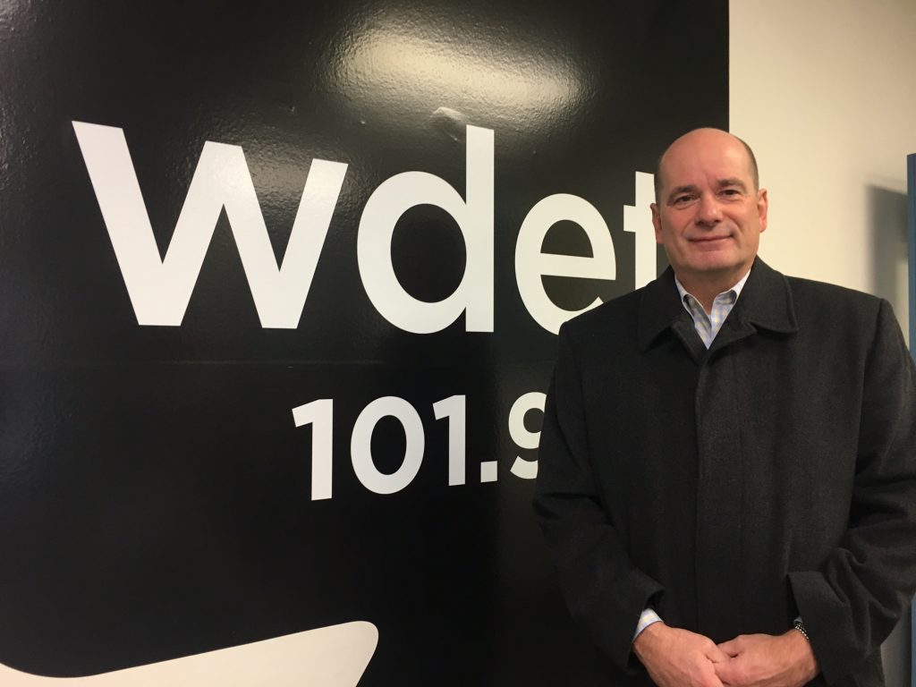 Nolan Finley smiles in front of the WDET logo