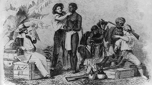 An African man being inspected for sale into slavery while a white man talks with African slave traders.