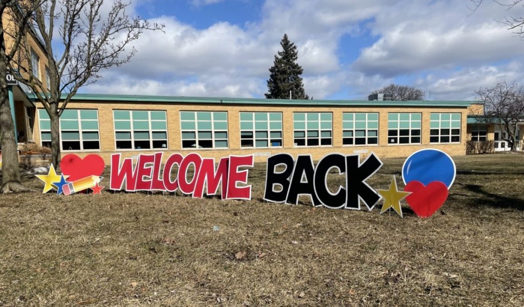 black and red sign that reads "welcome back" in front of a school building