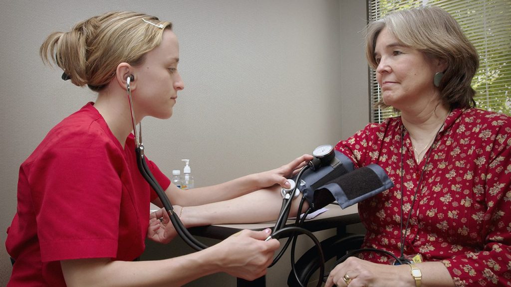 woman in scrubs takes another woman's blood pressure