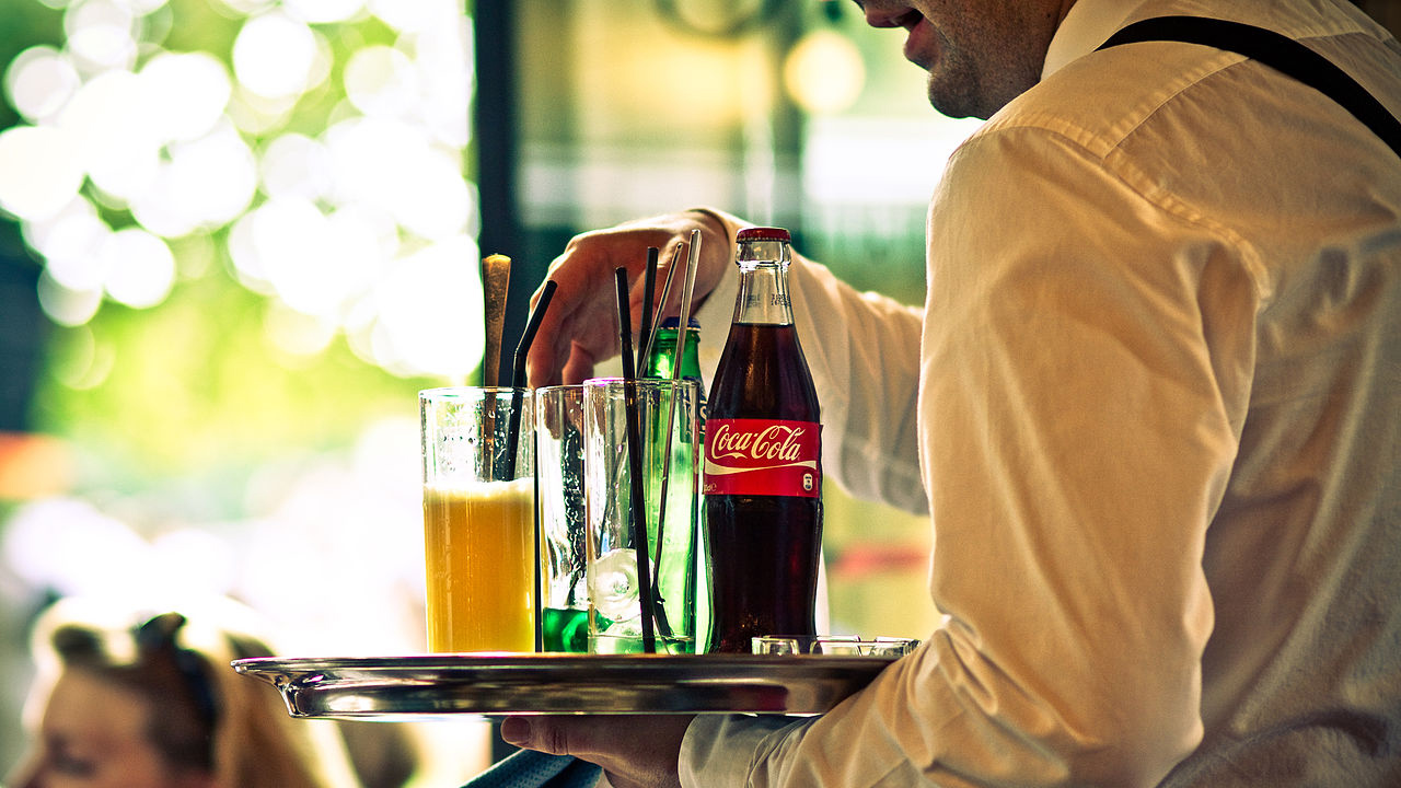 A server carries a tray with drink glasses and a Coke bottle.