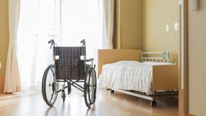 A wheelchair next to an empty bed in a nursing home