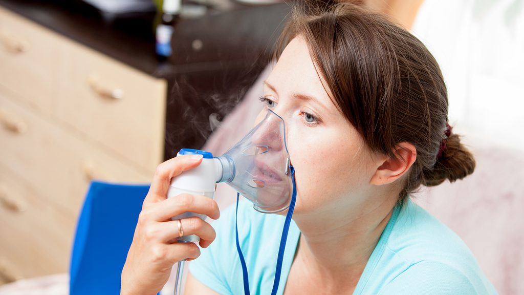 Young woman doing inhalation with a nebulizer at home