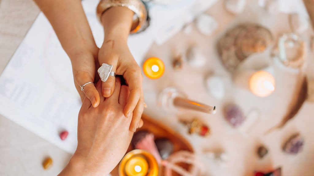 Two people hold hands with one wearing a silver ring above candles