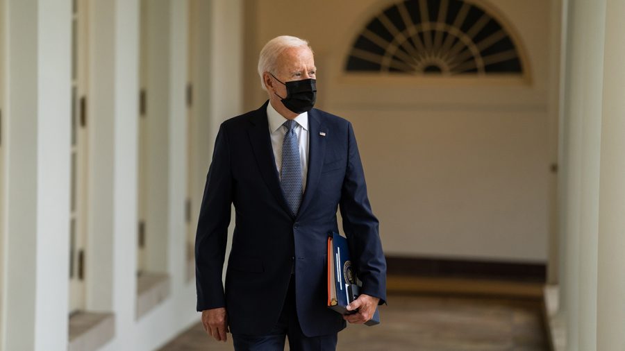 President Biden walks along the West Colonnade with a folder in his left hand.