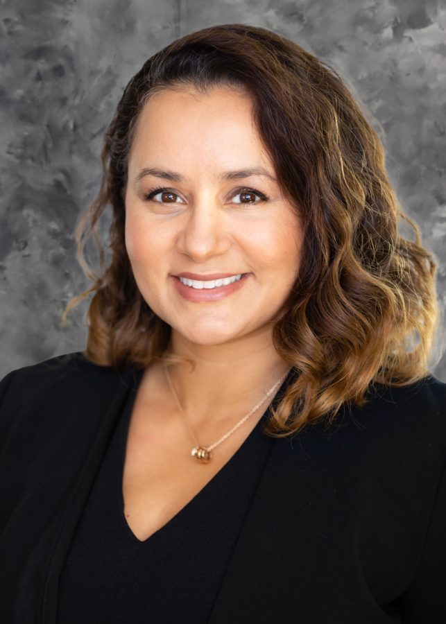 A photo of Natasha Bagdasarian wearing a black top standing against a gray background.