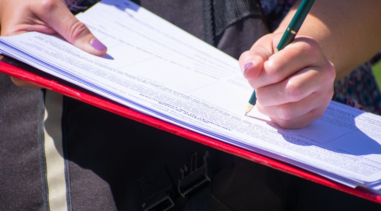 A person signs a petition for a ballot proposal on a clipboard.