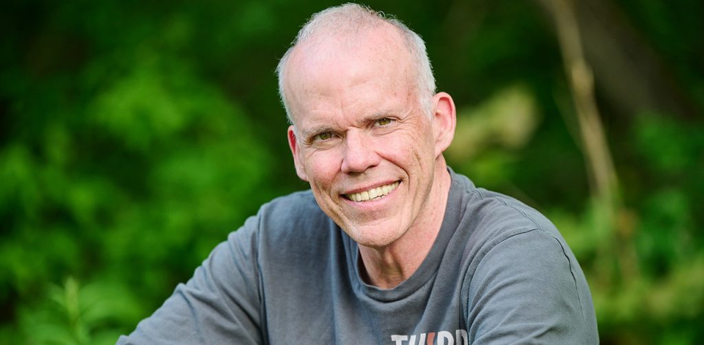 The author Bill McKibben wearing a gray shirt and sitting outdoors