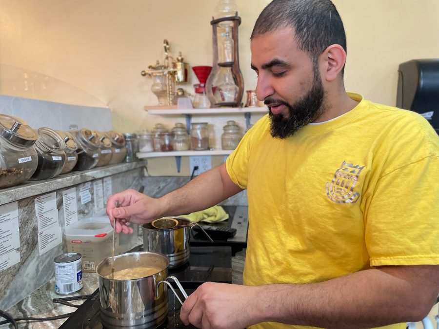 Fares Abdulmalek wears a yellow T-shirt and stands at an espresso bar at Finjan Cafe.