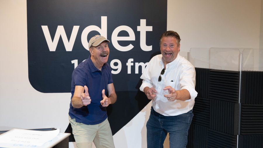 Under The Radar Michigan co-hosts Tom Daldin and Jim Edelman stand in front of the black WDET logo
