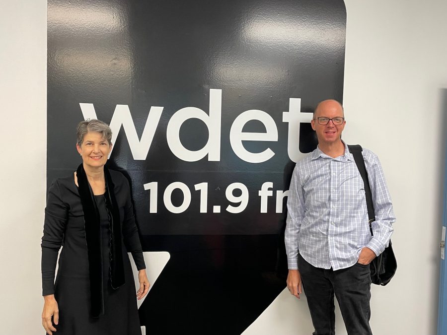 Leslie Ann Pilling and Rob St. Mary smile in front of the WDET logo.