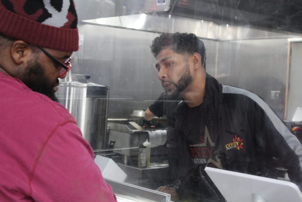 Syeed Choudhury peers through bullet-proof glass to help a customer
