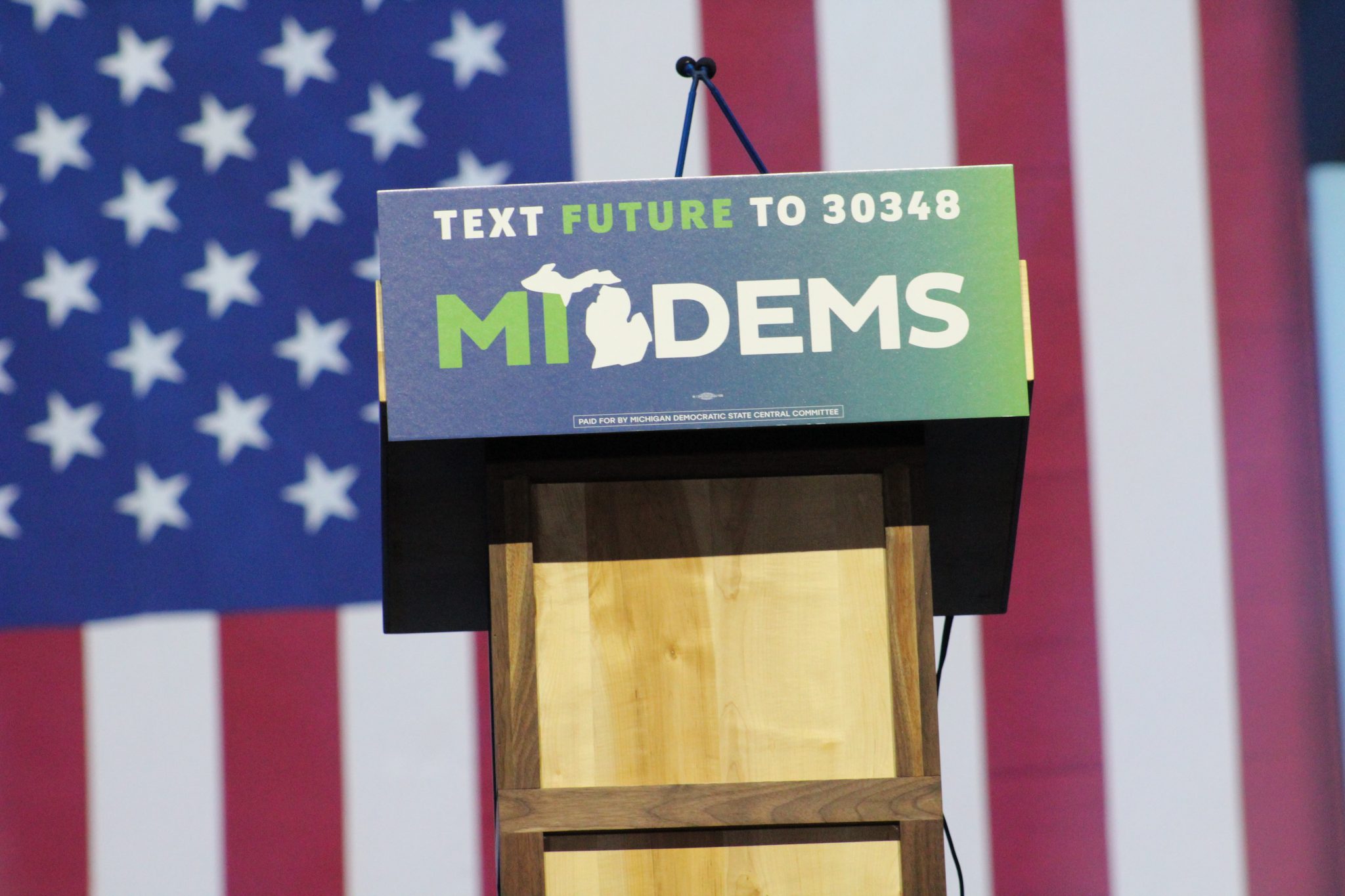 podium that reads "MI Dems" in front of an American flag