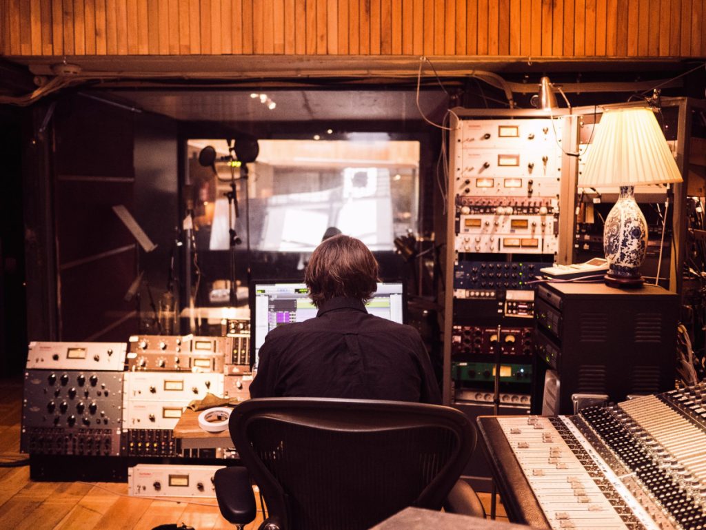 a person sits in a recording studio surrounded by audio equipment