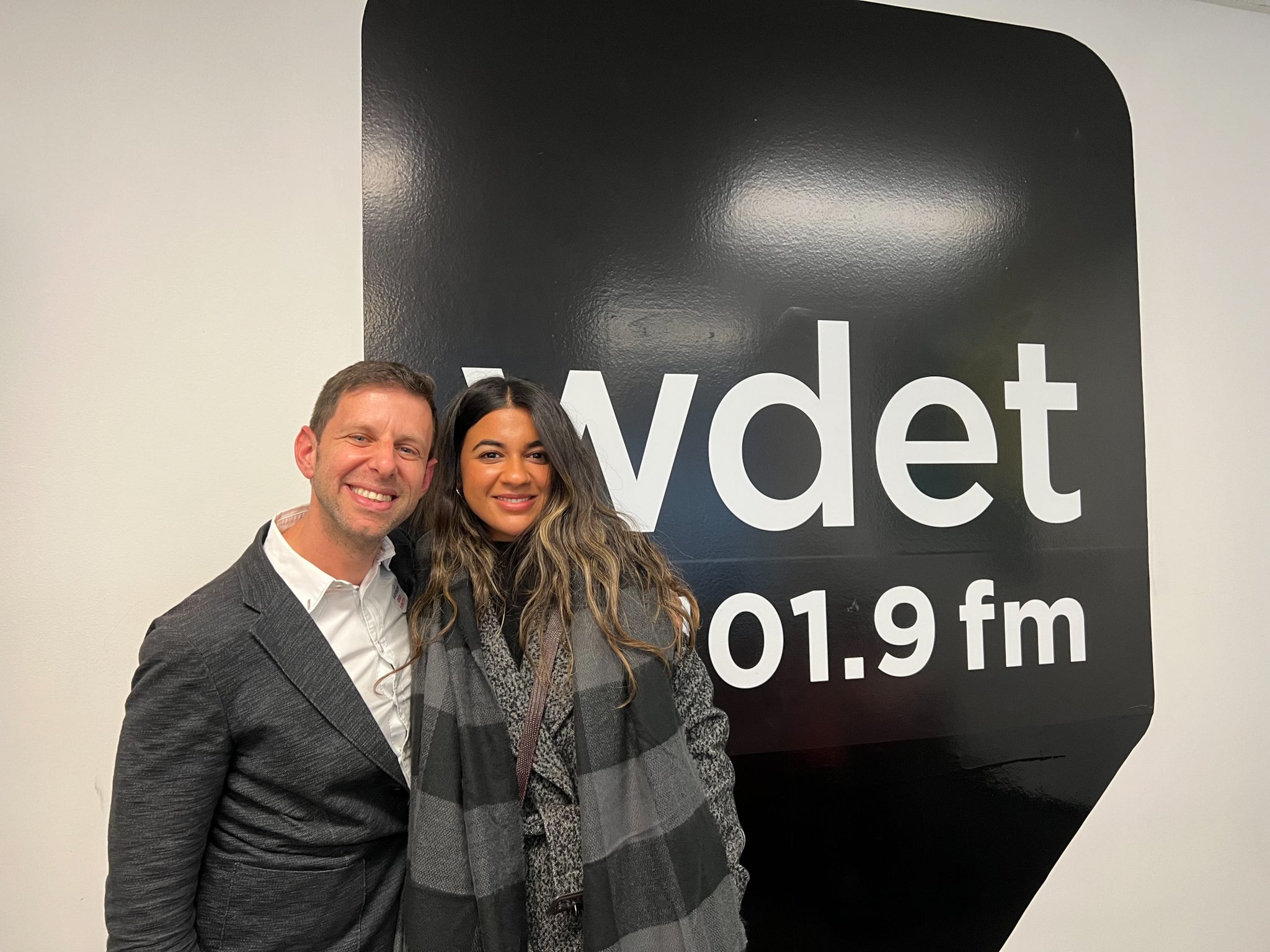 Yuval Sharon and Amina Edris smile in front of WDET's logo at our studios in November 2022