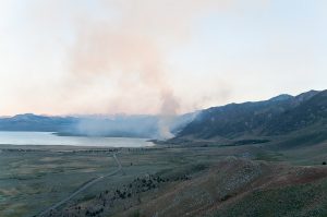 a forest fire with smoke covering an area near a lake, hills and mountains