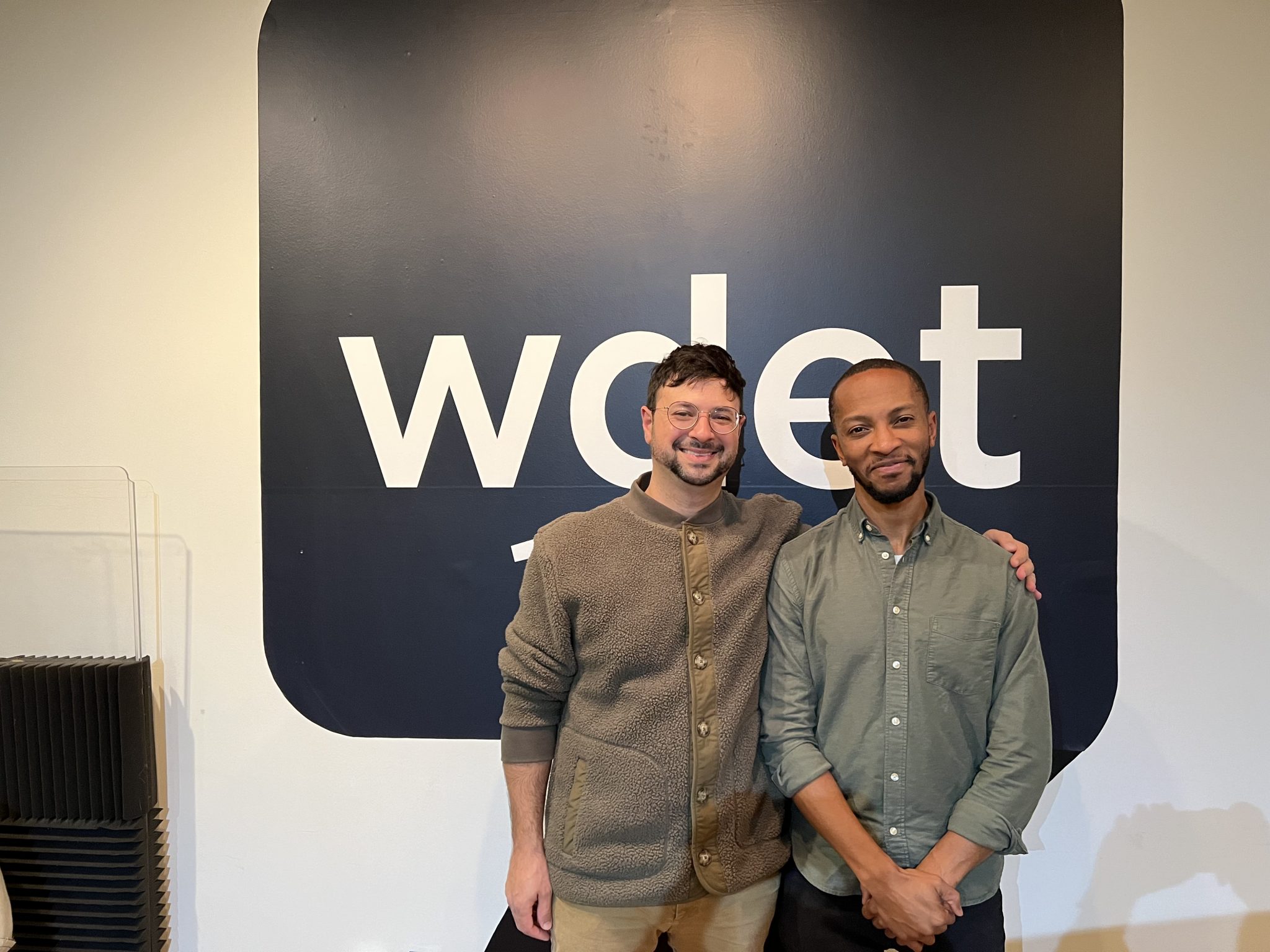 Michael Malis and Marcus Elliot smile in front of the WDET logo