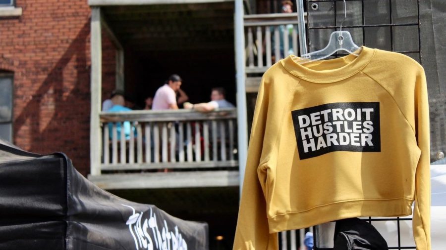 a yellow sweatshirt with "Detroit hustles harder" printed on it hangs on an outdoor fixture