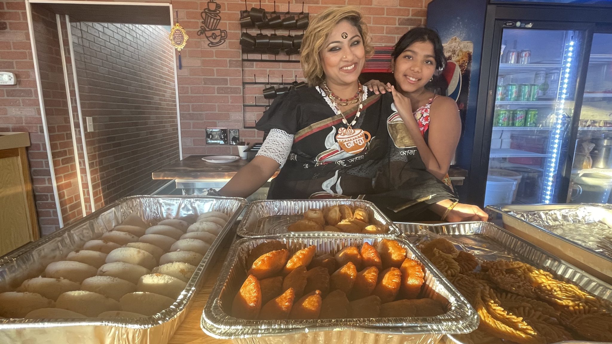 A woman and her daughter smile with several trays of food