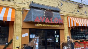 exterior of yellow brick building with a red sign that reads "Avalon International Breads"