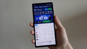 a hand holds up a smartphone displaying Sportsbook Online Betting