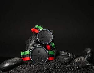 two watches with green, black and red striped wristbands and black faces with black hands and numbers