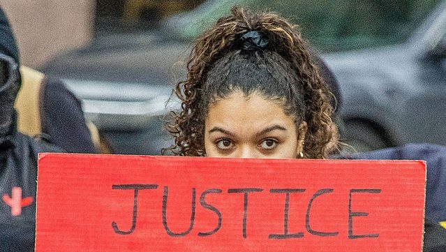 Black woman holds up a red sign that reads "justice"
