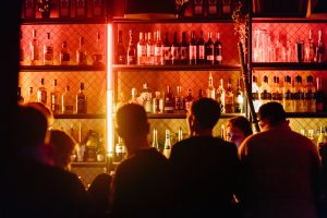 people standing at a bar with shelves of liquor