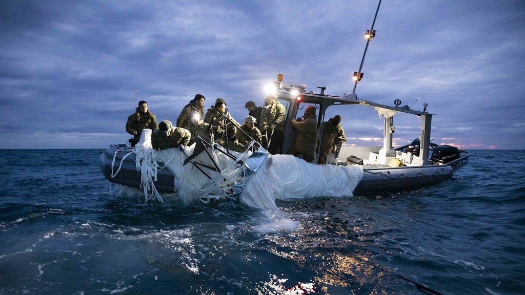 people in jackets bring a deflated white balloon onboard a ship from a body of water at night