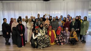 A large group of hijabi women pose for a picture in a meeting space