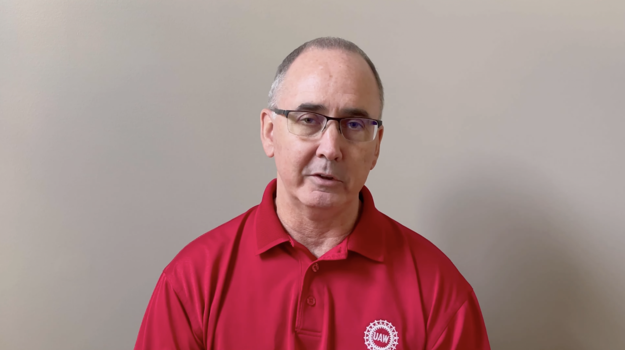 a white man in a red UAW polo shirt wearing glasses