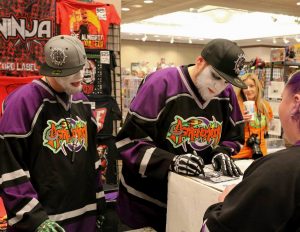 people wearing white face paint, gray baseball hats and neon hockey jerseys sign autographs at a convention