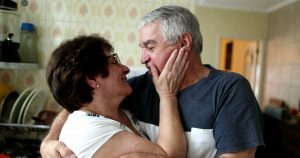 an older couple smiles at each other in their home