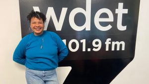 Dr. Jessica Moorman smiles in front of the WDET logo
