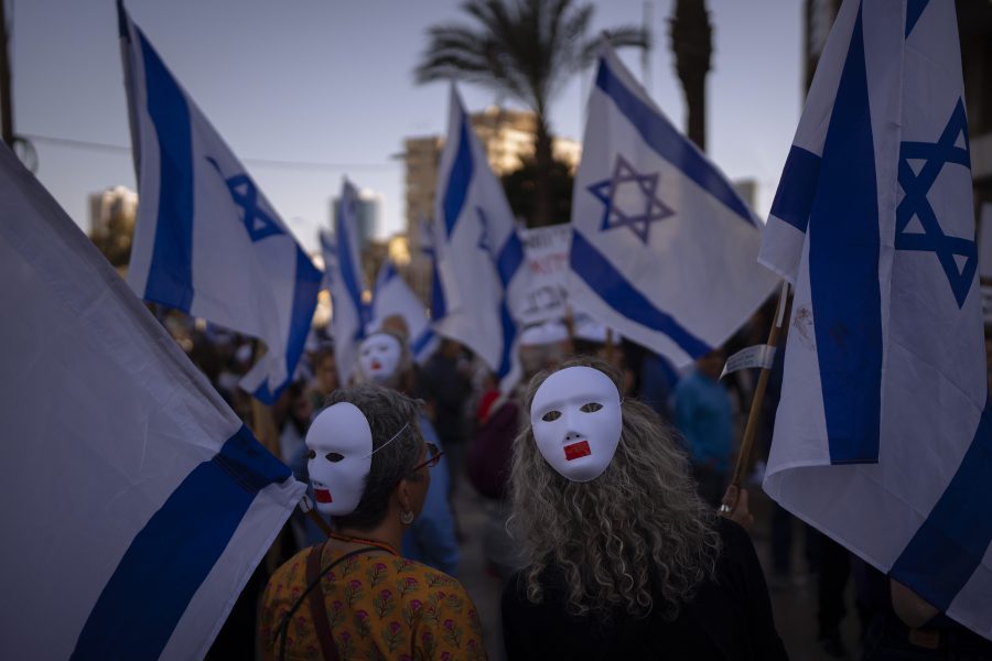 Demonstrators wear masks and wave Israeli flags during a protest against plans by Prime Minister Benjamin Netanyahu's government to overhaul the judicial system in Tel Aviv, Israel, Tuesday, March 28, 2023.