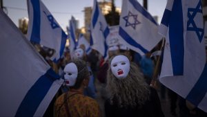 Demonstrators wear masks and wave Israeli flags during a protest against plans by Prime Minister Benjamin Netanyahu's government to overhaul the judicial system in Tel Aviv, Israel, Tuesday, March 28, 2023.