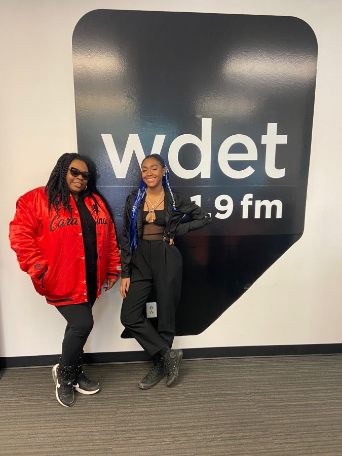 Two Black women smile in front of the WDET logo