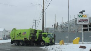 A green garbage truck pulls into WM's transfer station on a snowy day.