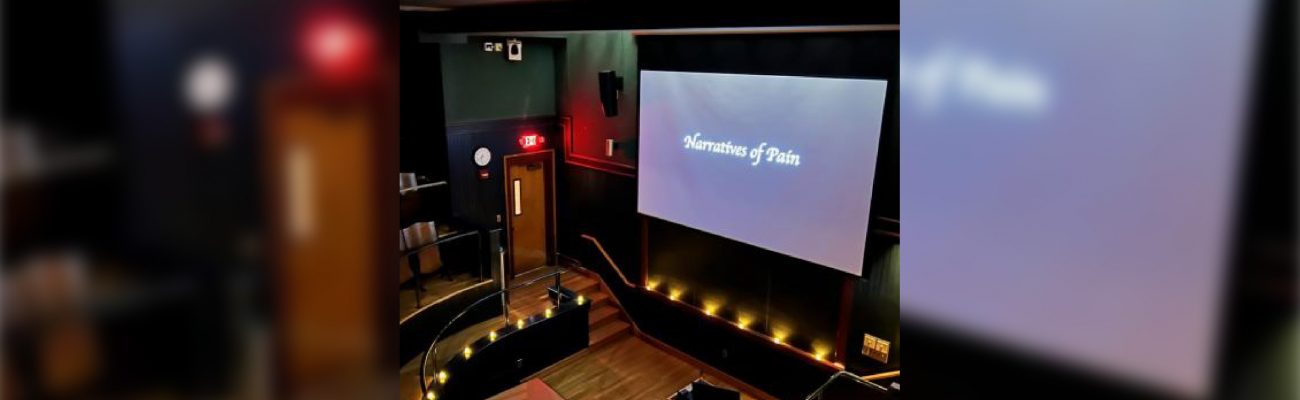 a dark auditorium lit by candles and a screen that reads "Narratives of Pain"