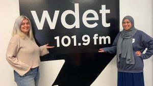 Eater Detroit editor Serena Maria Daniels and WDET reporter Nargis Rahman post in front of a WDET logo.