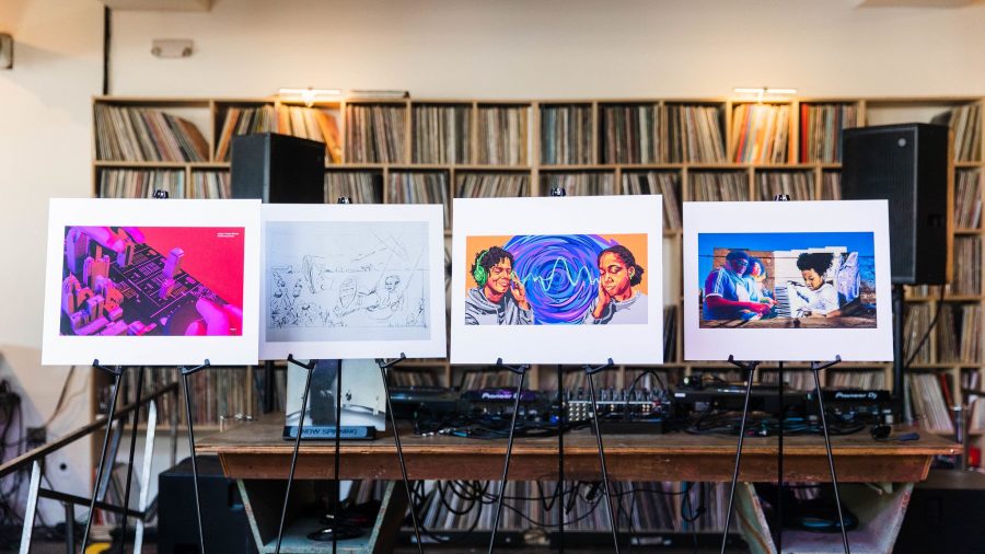 Four colorful illustrations are displayed on easels in front of shelves of vinyl records