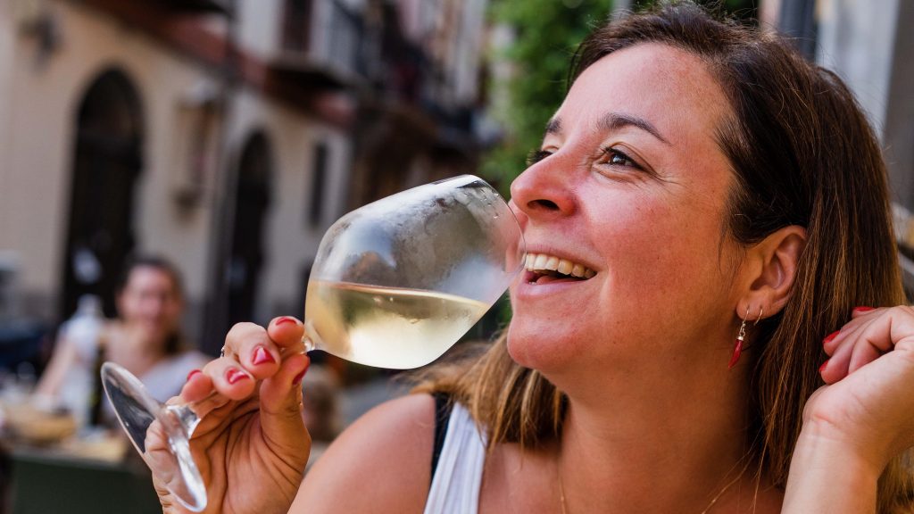 Katie Parla smiles and drinks a glass of white wine in Italy