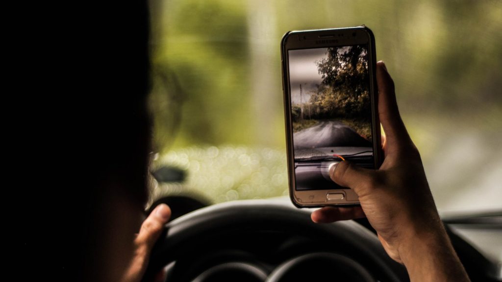 Man looks at cell phone in camera mode while driving.