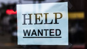 A help wanted sign hanging from a door.