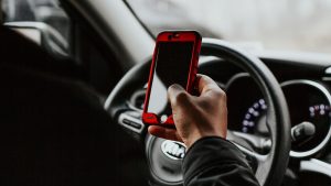 person holding an iPhone behind the steering wheel of a car