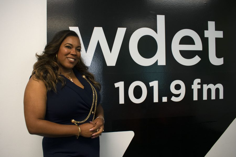 Loren Hicks smiles in front of the WDET logo