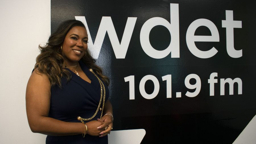 Loren Hicks smiles in front of the WDET logo