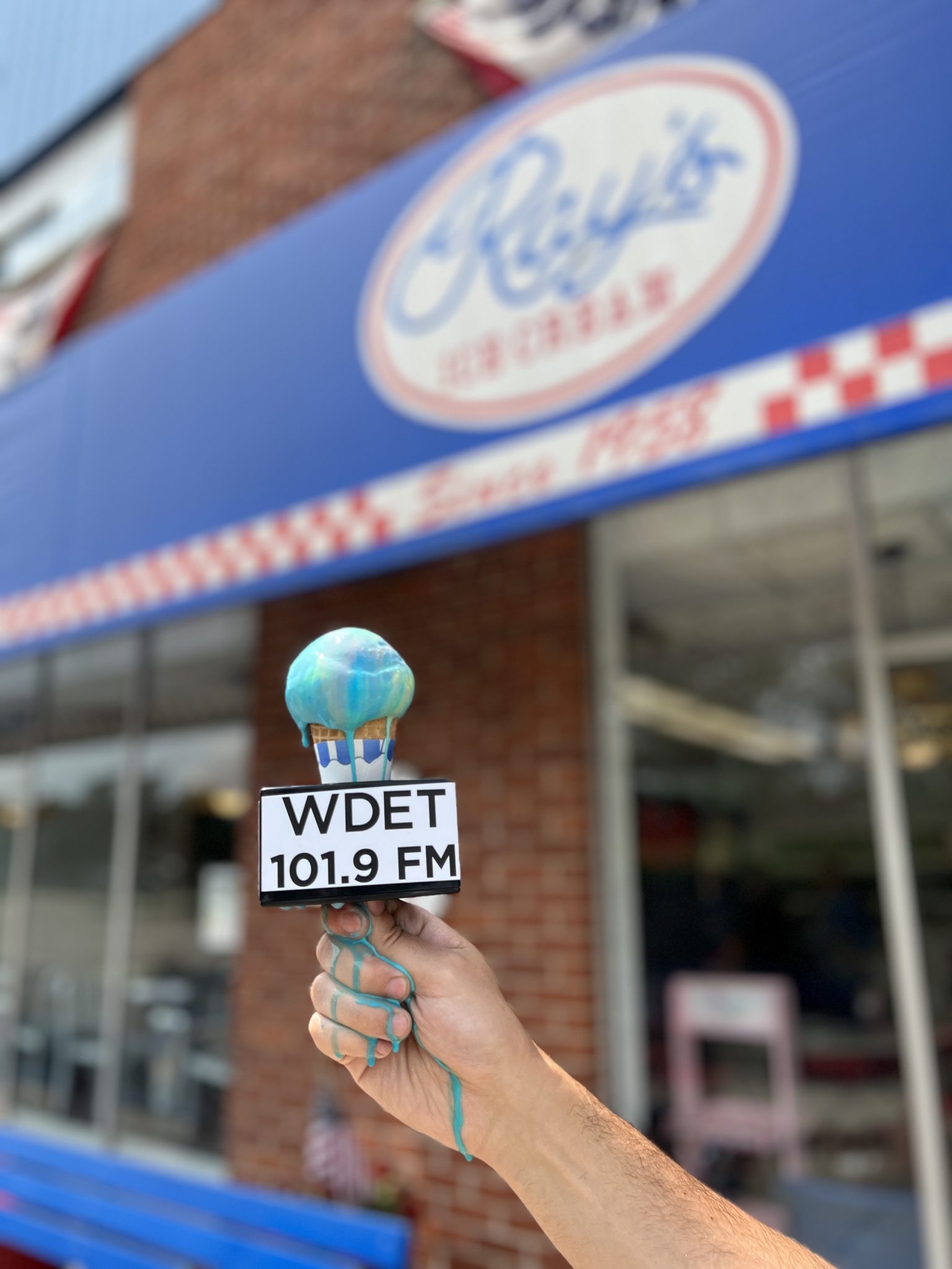 A cone of Superman ice cream with a WDET microphone flag melts down a reporters hand.