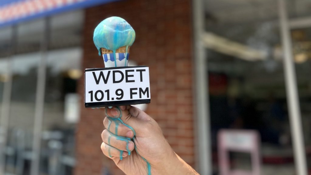 A cone of Superman ice cream with a WDET microphone flag melts down a reporters hand