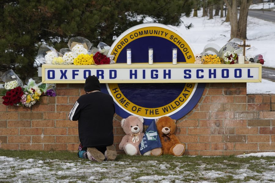 A well wisher kneels to pray at a memorial on the sign of Oxford High School in Oxford, Mich., Wednesday, Dec. 1, 2021.